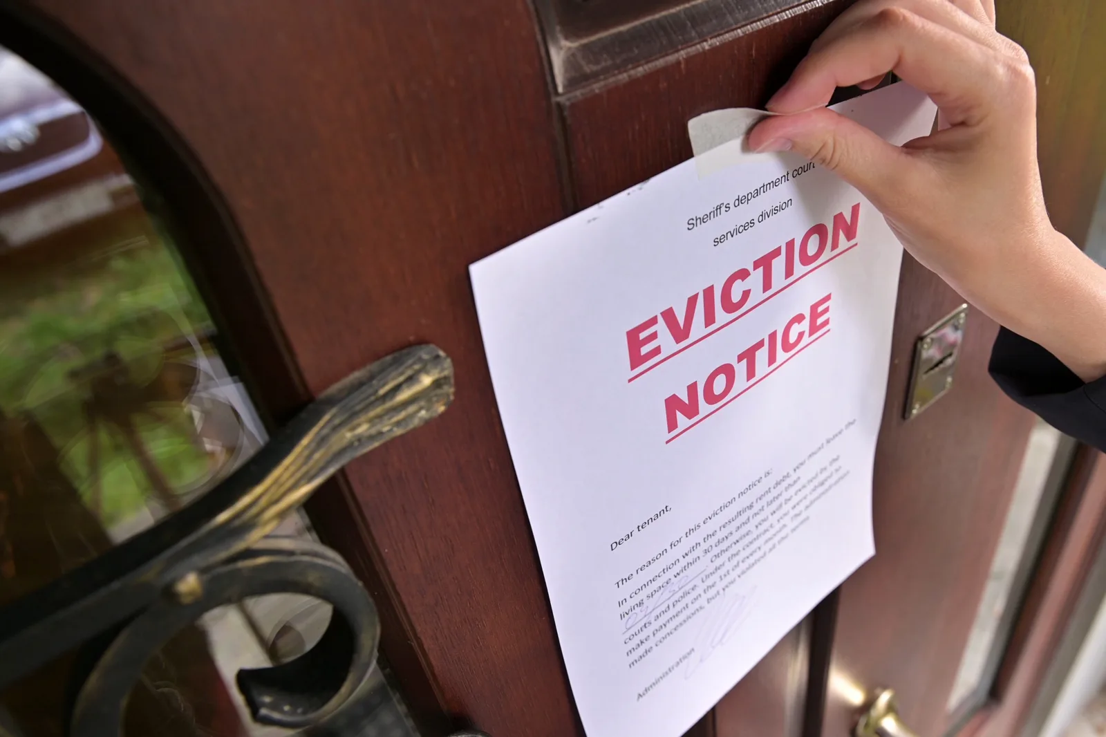 A hand taping an eviction notice to the front door of a home